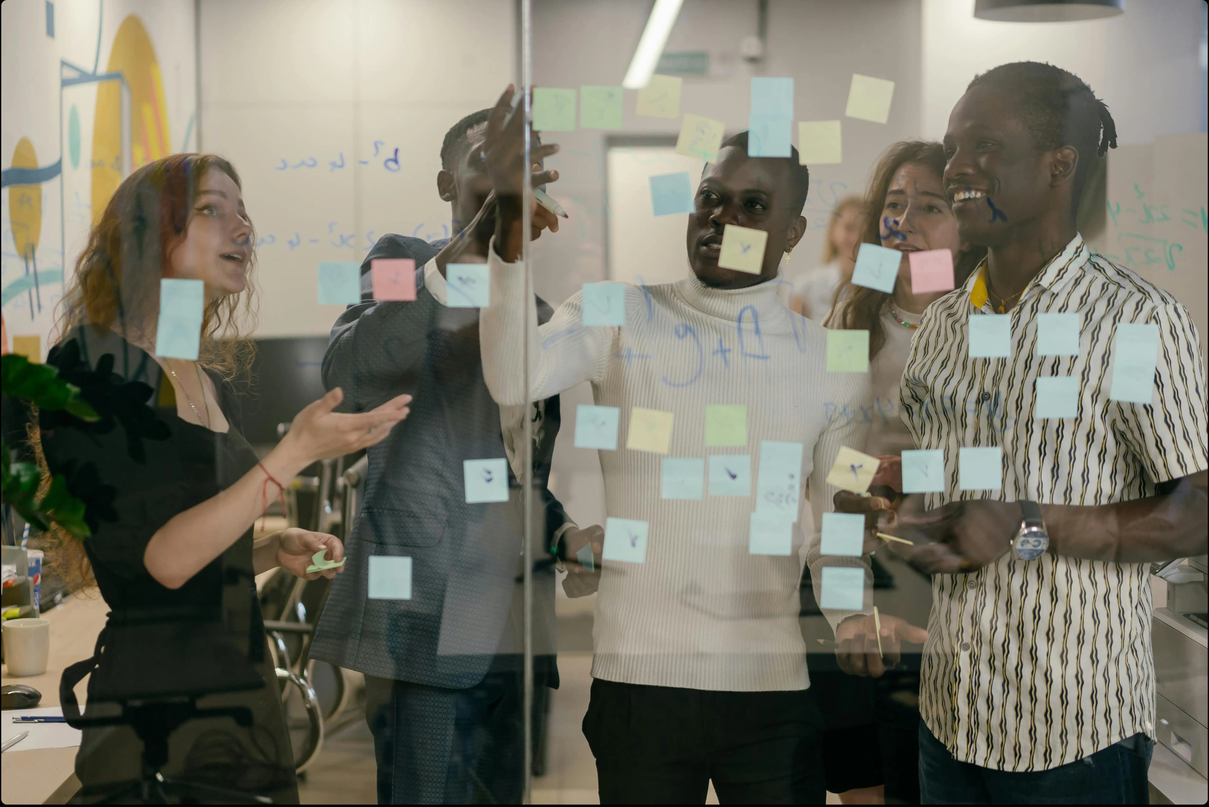 Group of colleagues standing in front of a glass panel organising post it notes that are stuck on the glass.